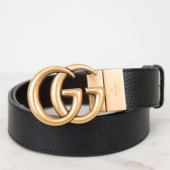 Black leather belt with gold Gucci buckle on a light background