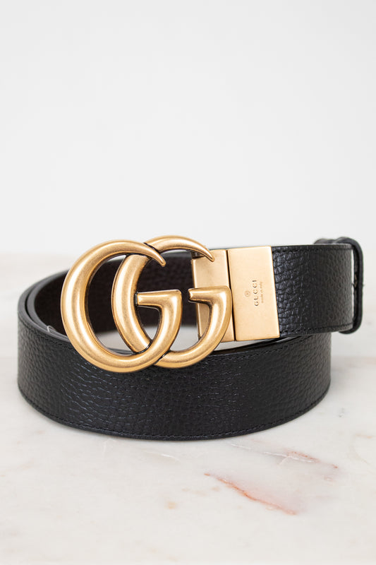 Black leather belt with gold Gucci buckle on a light background