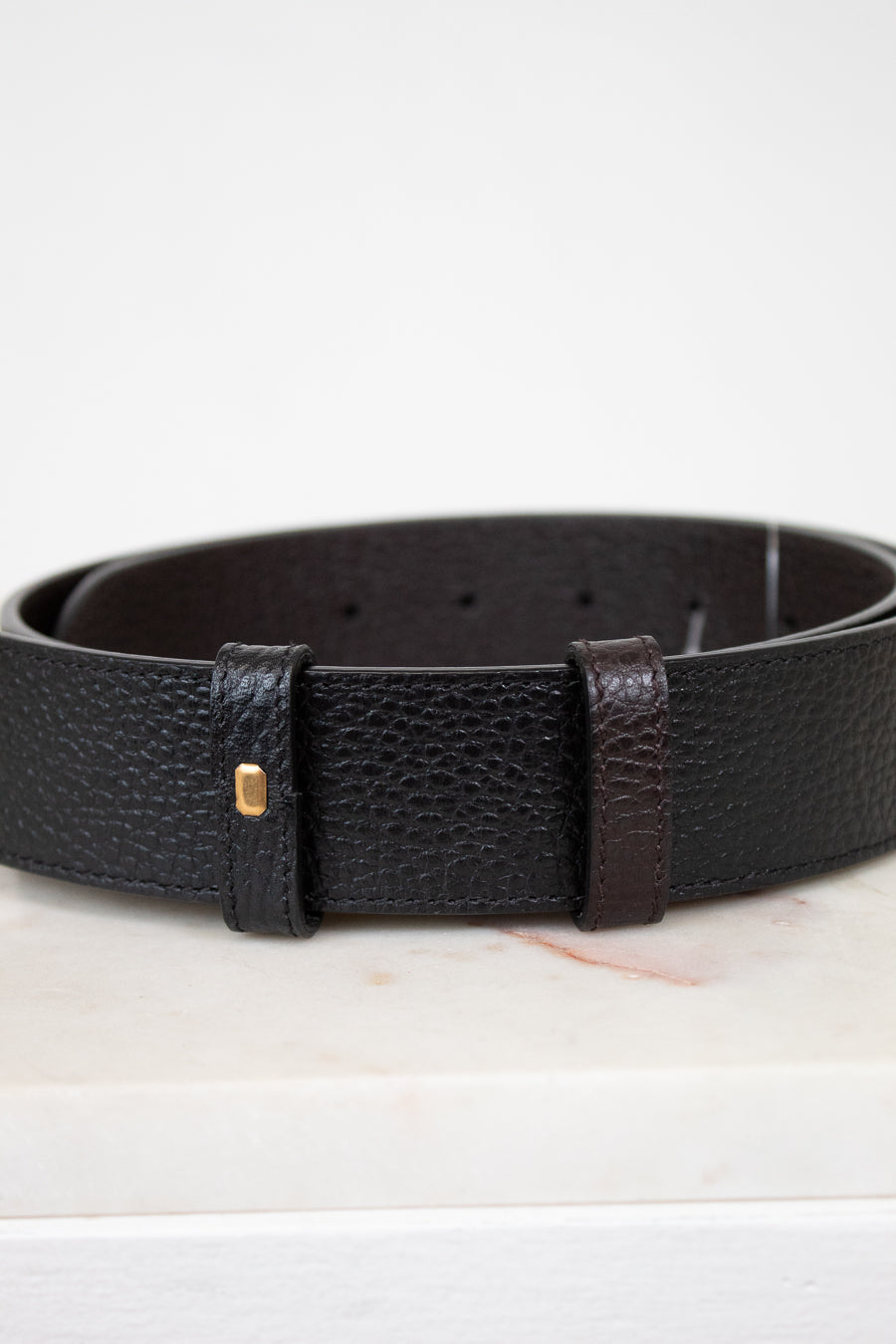 Black leather belt with a gold buckle on a white background
