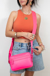 Person wearing an orange top, denim shorts, and a pink crossbody bag against a plain background