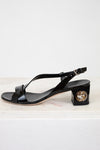 Black sandal with a block heel and decorative buckle on a white background