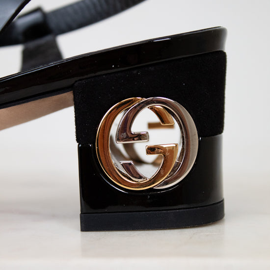 Black high-heeled sandal with a gold and white logo on a white background