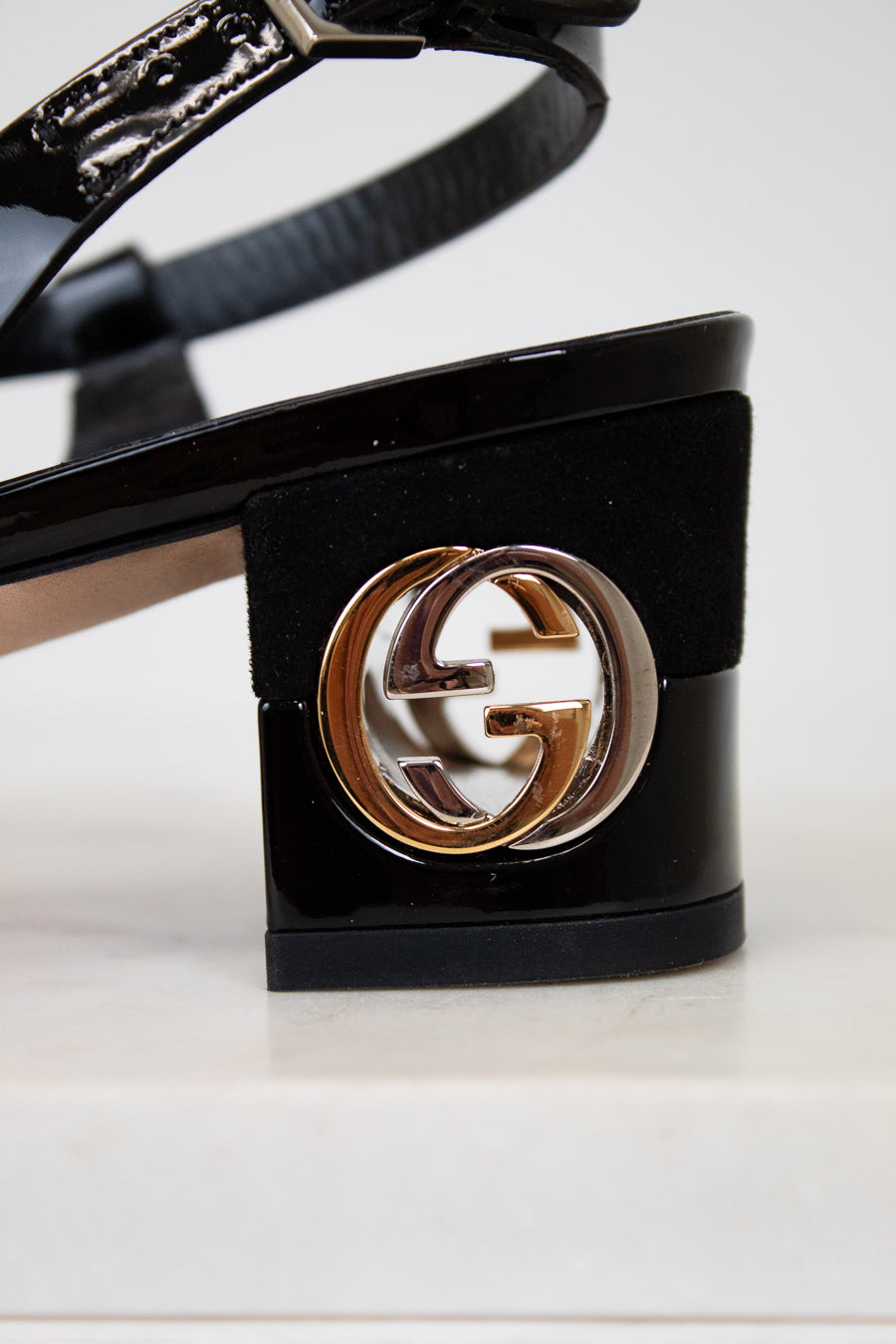 Black high-heeled sandal with a gold and white logo on a white background