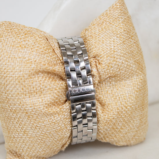 Silver watch band on a textured beige pillow with a white background