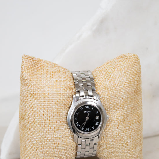 Silver watch on a textured beige pillow against a white background
