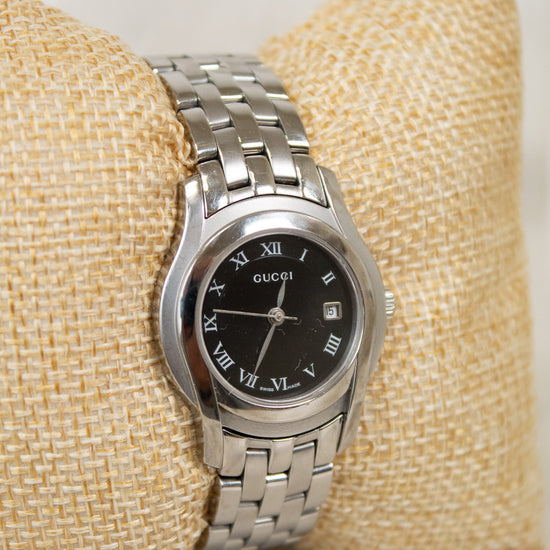 Silver watch with a black dial on a beige cushion