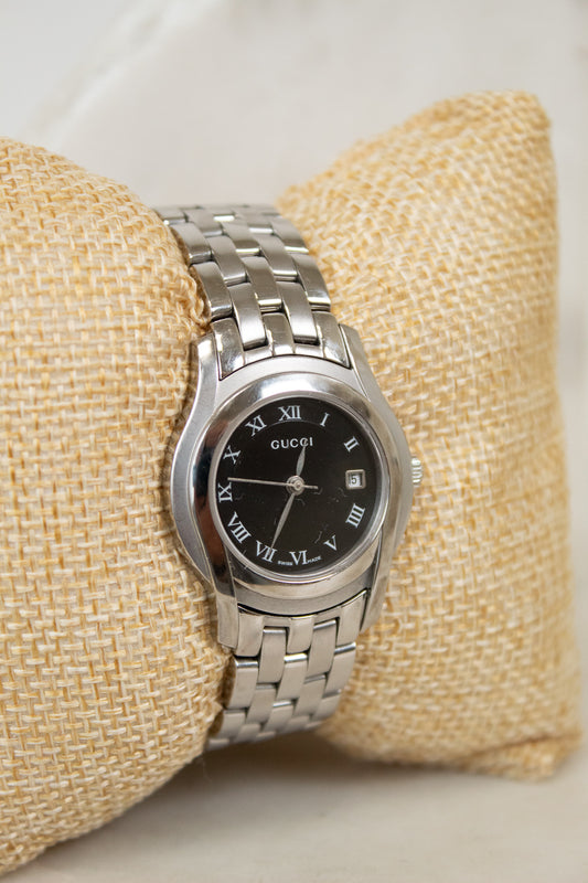 Silver watch with a black dial on a beige cushion