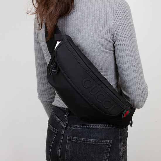 Person wearing a black Gucci bag on a plain background