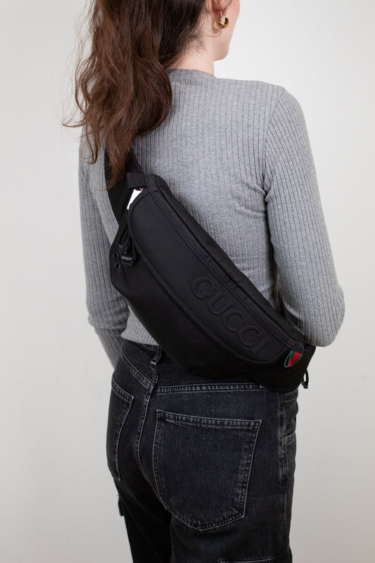 Person wearing a black Gucci bag on a plain background