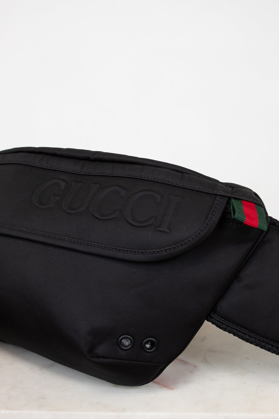 Black Gucci waist bag with logo and color stripe on a light background