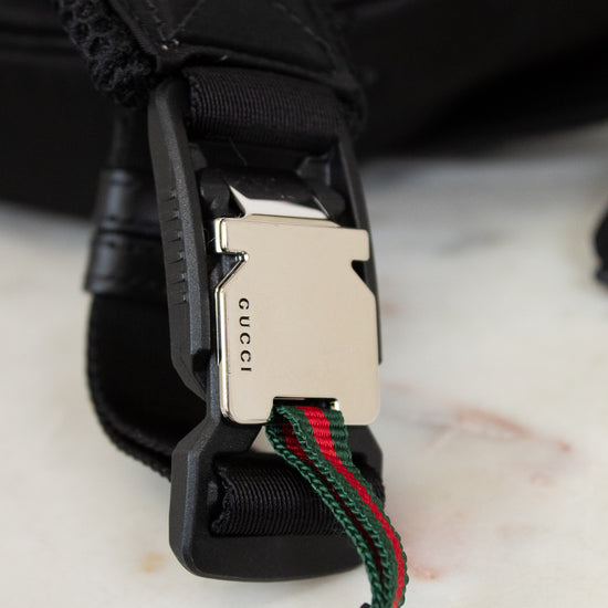 Close-up of a Gucci belt with a black buckle and green and red webbing on a light background.