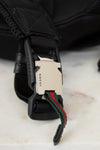 Close-up of a Gucci belt with a black buckle and green and red webbing on a light background.