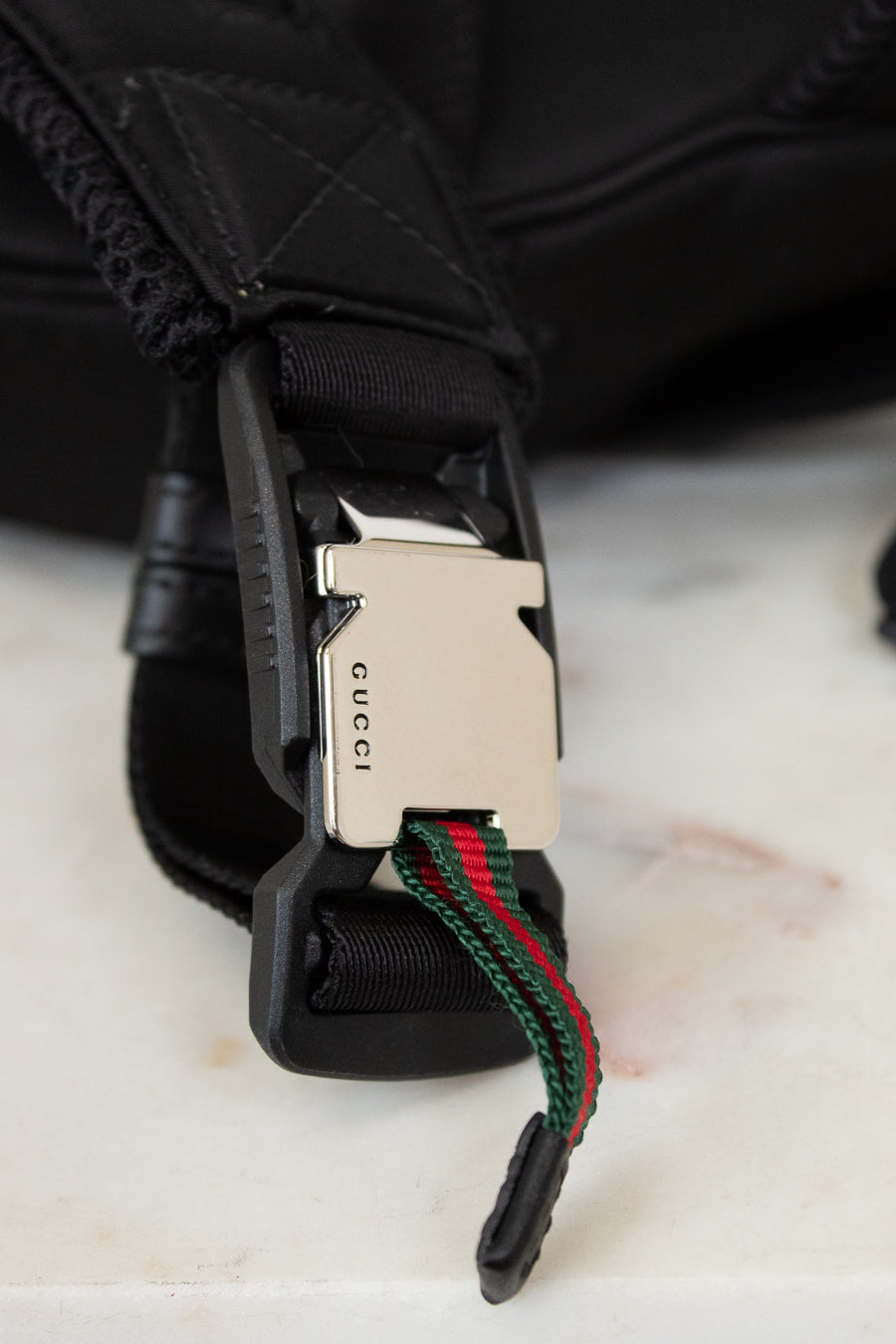 Close-up of a Gucci belt with a black buckle and green and red webbing on a light background.