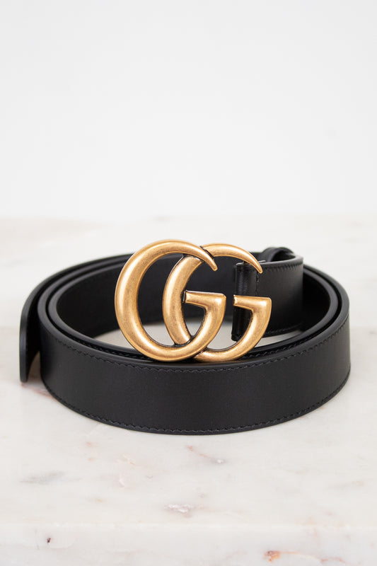 Black Gucci belt with gold logo on a white marble surface
