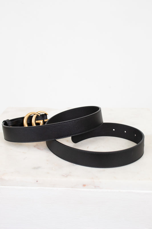 Black leather belt with a gold buckle on a white marble surface