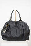 A black leather shoulder bag with an embossed monogram pattern, gold-tone hardware, and a hanging interlocking G logo charm, displayed on a white pedestal against a white background.