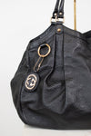 A black leather shoulder bag with an embossed monogram pattern, featuring gold-tone hardware, a hanging keychain with a Gucci logo patch, and a gold ring detail, shown against a plain white background.