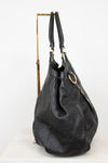 A black leather  handbag with an embossed monogram pattern, displayed on a gold metal stand against a white background.
