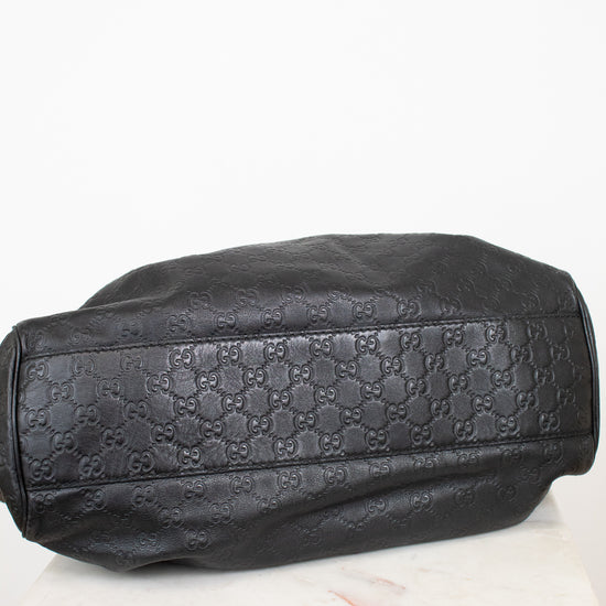 A black leather handbag with an embossed Gucci GG monogram pattern, resting on a white marble surface against a white background.