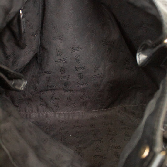 Close-up view of the interior lining of a black leather handbag, showing a dark gray patterned fabric lining with a small brand tag near the top.