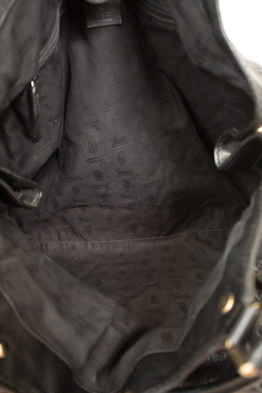 Close-up view of the interior lining of a black leather handbag, showing a dark gray patterned fabric lining with a small brand tag near the top.