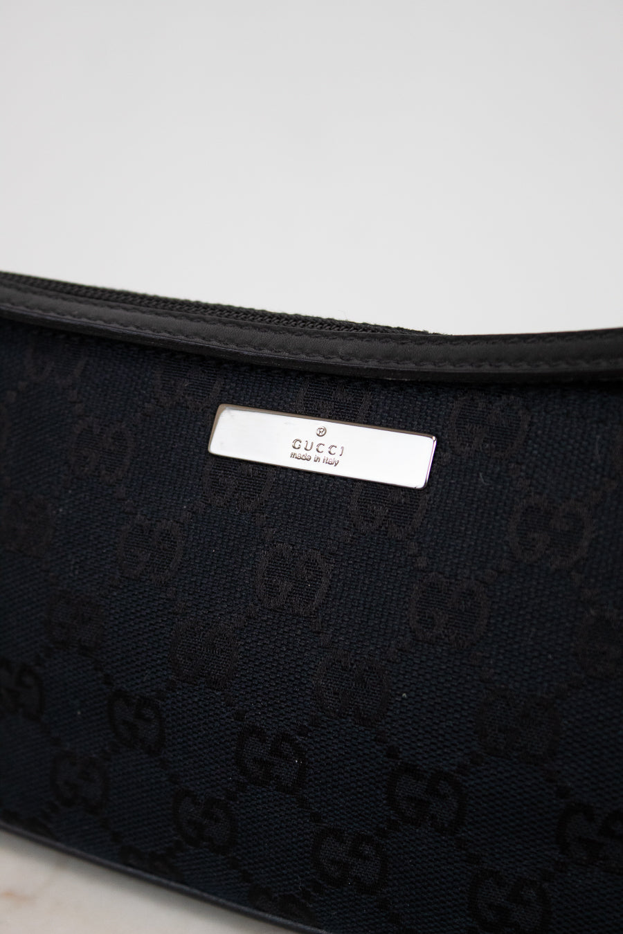 Close-up of black Gucci bag with logo pattern on a light gray background
