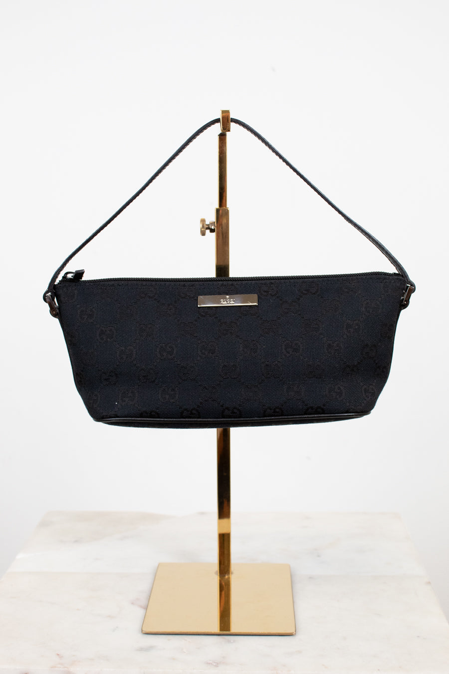 Black handbag on a gold stand against a white background