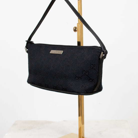 Black handbag on a gold stand against a white background
