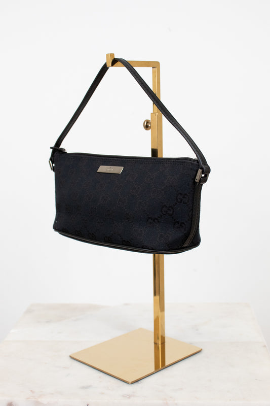 Black handbag on a gold stand against a white background