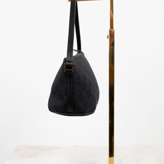 Black handbag on a gold stand against a white background