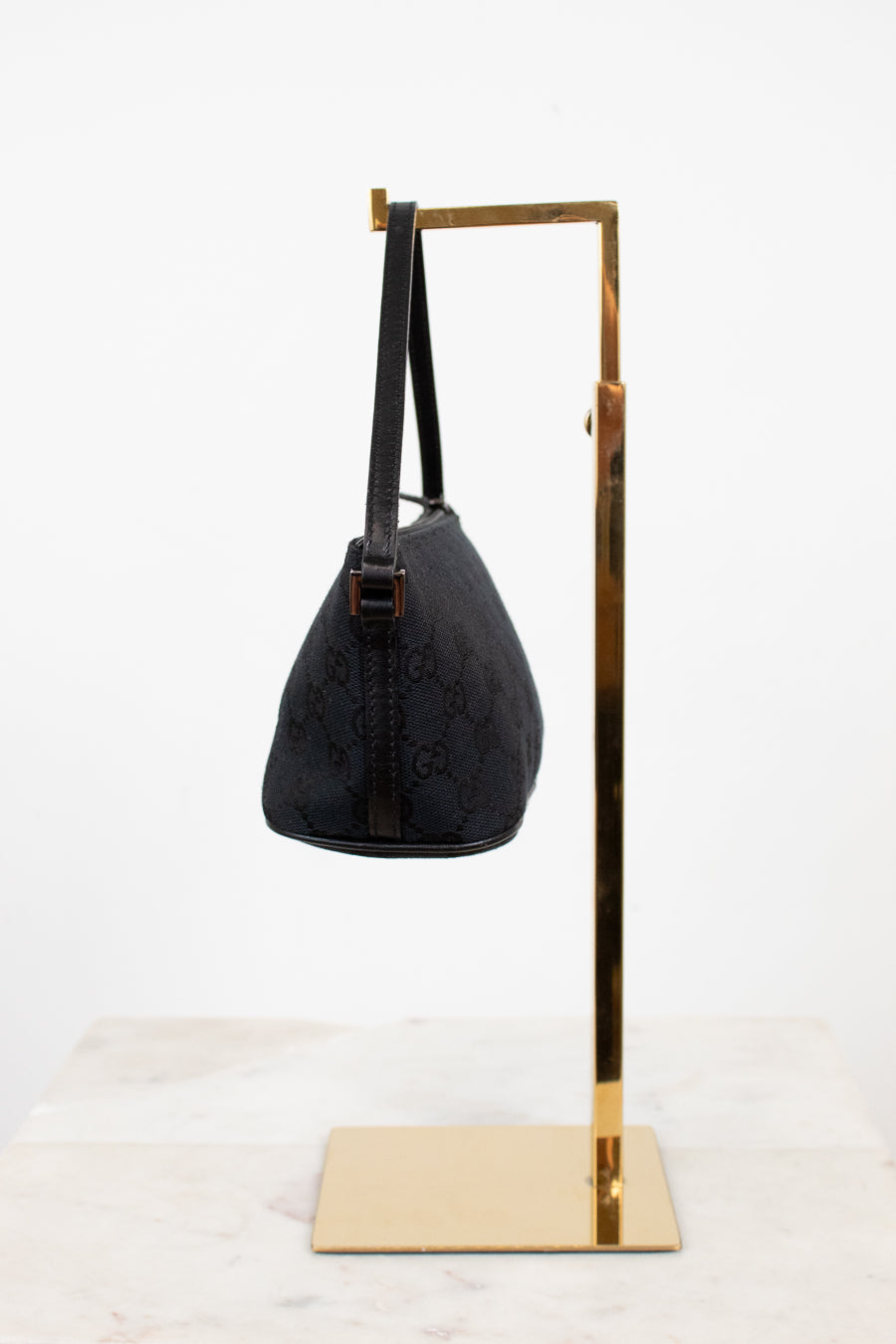 Black handbag on a gold stand against a white background