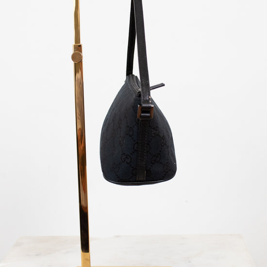 Black handbag on a gold stand against a white background