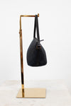Black handbag on a gold stand against a white background