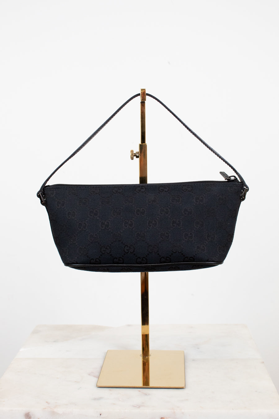 Black handbag on a gold stand against a white background