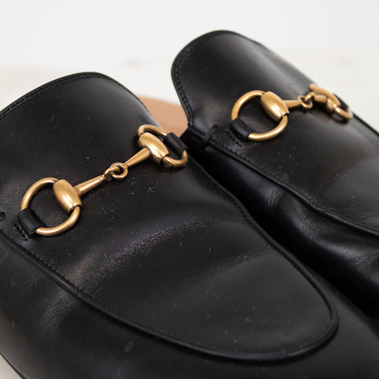 Black leather slip on mules with gold hardware on a light background