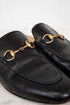 Black leather slip on mules with gold hardware on a light background