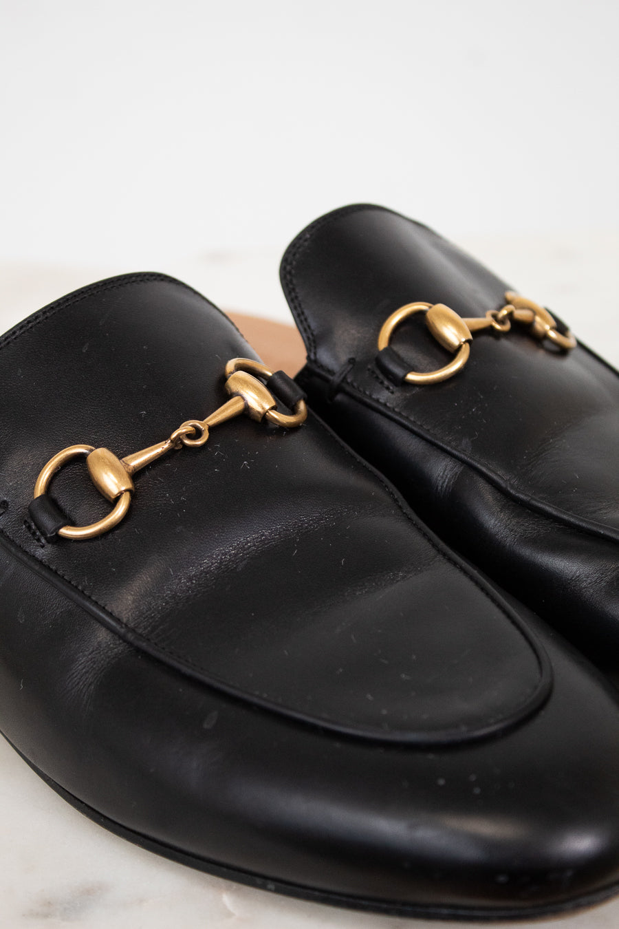 Black leather slip on mules with gold hardware on a light background
