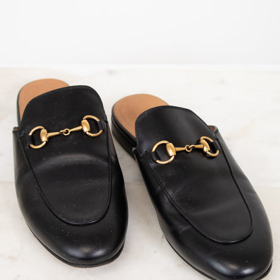 Pair of black leather slip on shoes with gold hardware on a light background