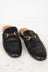 Pair of black leather slip on shoes with gold hardware on a light background