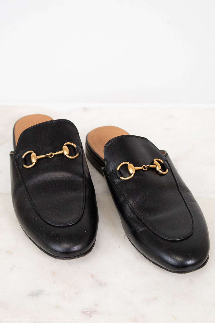 Pair of black leather slip on shoes with gold hardware on a light background