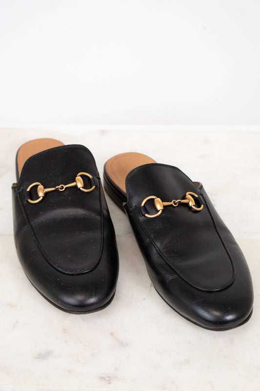 Pair of black leather slip on shoes with gold hardware on a light background