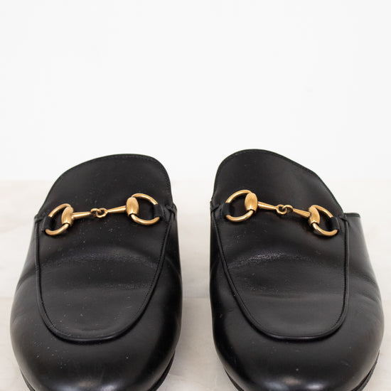 Pair of black leather slip on mules with gold hardware on a white background