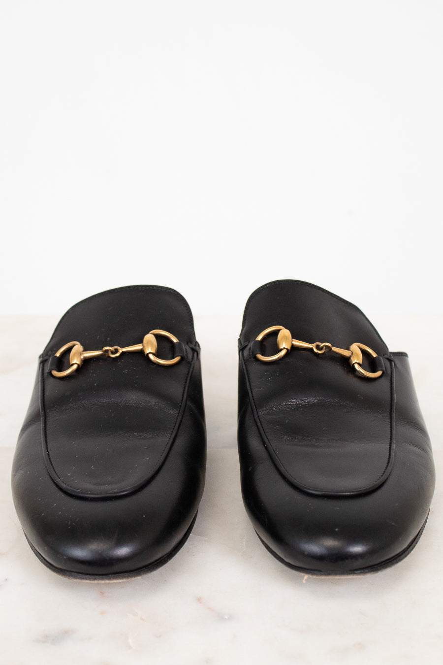 Pair of black leather slip on mules with gold hardware on a white background