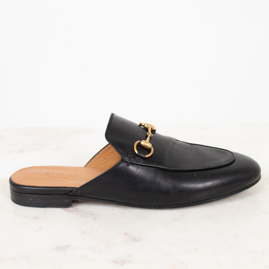 Black loafer slip-on shoe with gold buckle on a white background