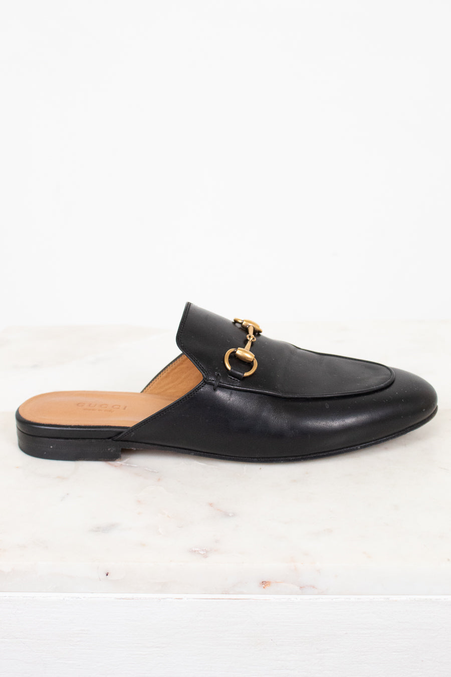 Black loafer slip-on shoe with gold buckle on a white background