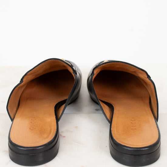 Pair of black leather mules with tan interior on a light background