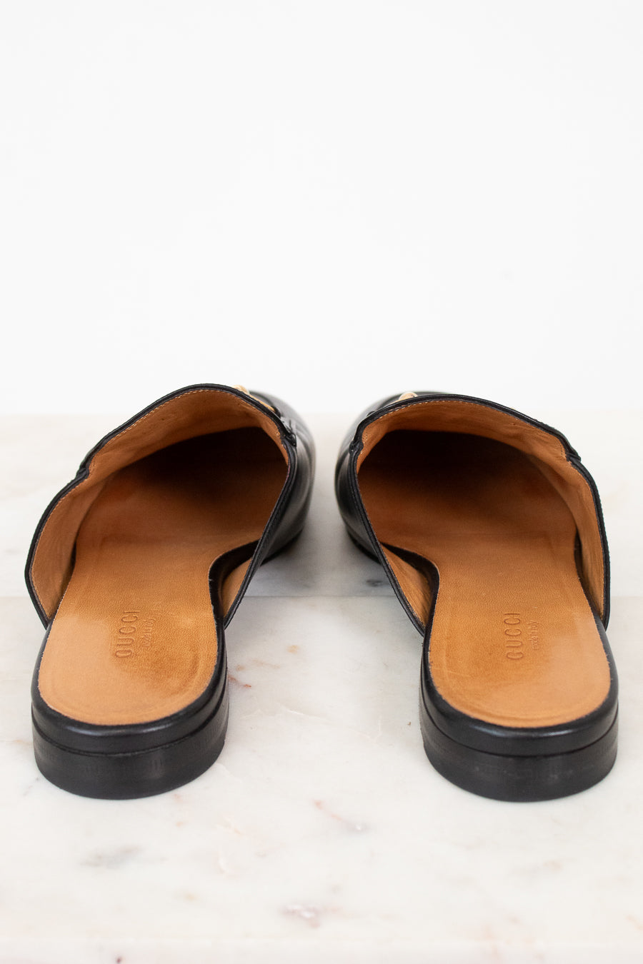Pair of black leather mules with tan interior on a light background