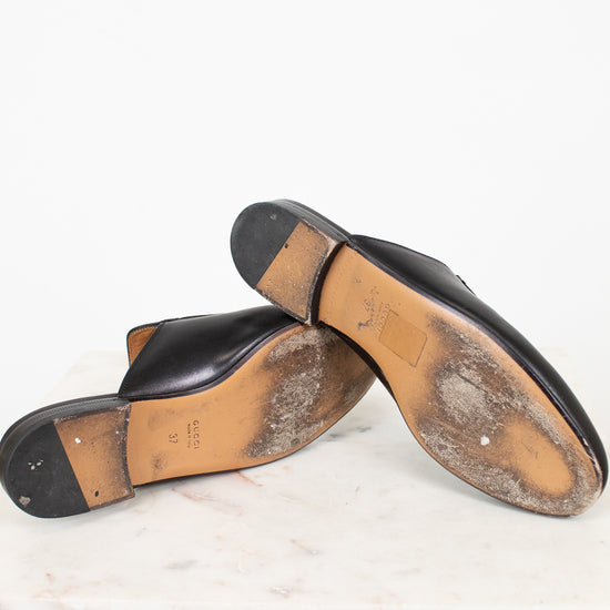 Pair of black leather shoes with tan soles on a white marble surface