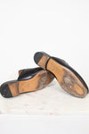 Pair of black leather shoes with tan soles on a white marble surface