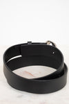 A black leather belt with a silver metal buckle, coiled on a white marble surface against a white background.